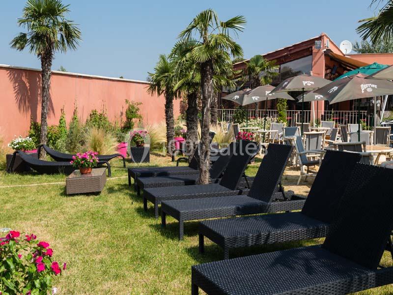 Chaises longues noires disposées sur une pelouse avec des palmiers, près d'une terrasse ombragée par des parasols.