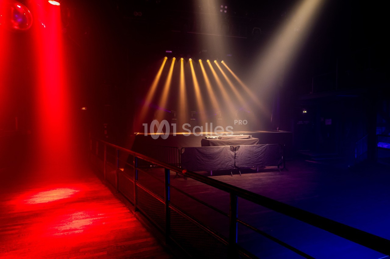 Scène de concert vide éclairée par des projecteurs rouges et jaunes dans une salle sombre.