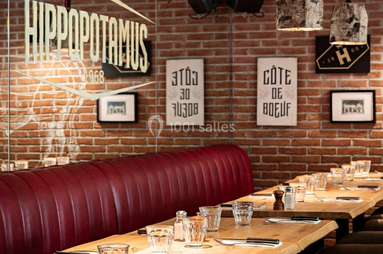 Salle de restaurant avec banquettes rouges, tables en bois dressées et décoration murale sur briques apparentes.