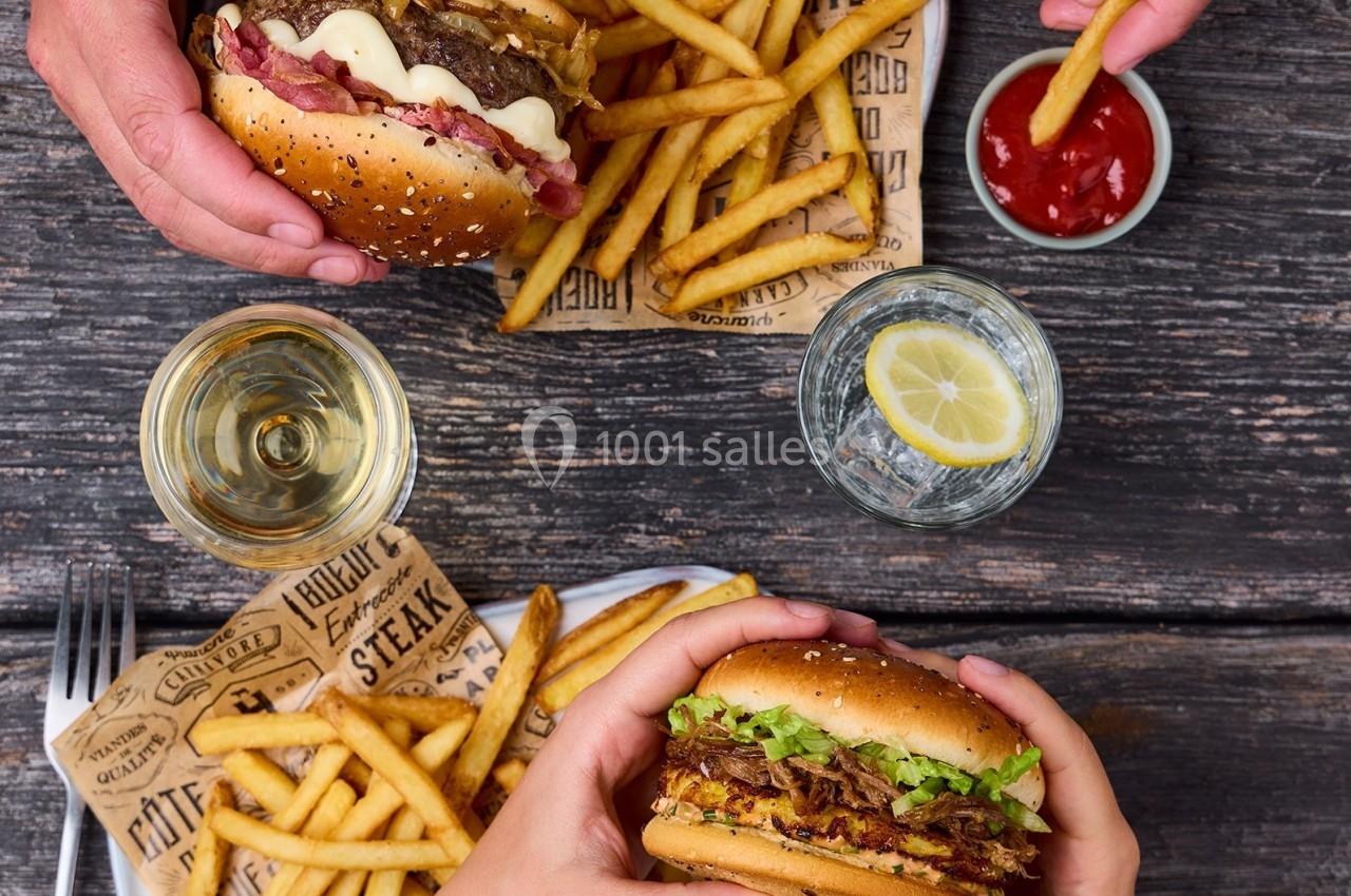Deux personnes dégustent des burgers accompagnés de frites et de boissons sur une table en bois.
