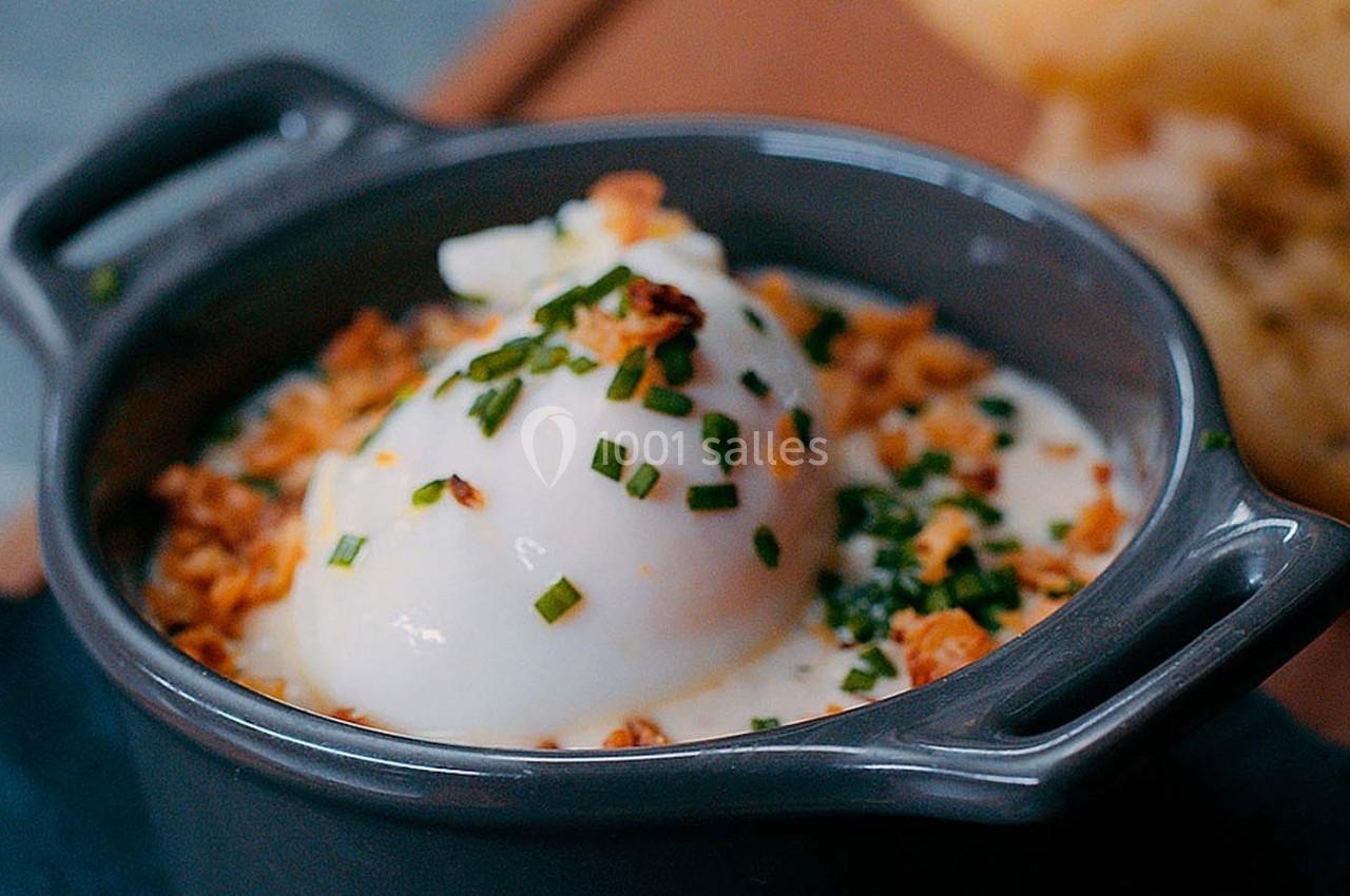 Œuf poché servi dans une petite cocotte avec une garniture de ciboulette et d'oignons croustillants.
