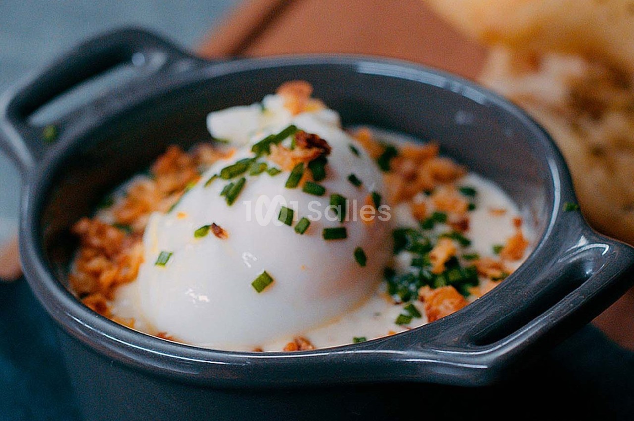 Œuf poché servi dans une petite cocotte avec une garniture de ciboulette et d'oignons croustillants.