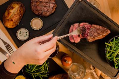 Miniature Location salle Boulogne-Billancourt (Hauts-de-Seine) - Hippopotamus Boulogne #26 Plat de viande rouge tranchée avec sauce au poivre, accompagné de frites, servi dans un plat ovale sur une table en bois.
