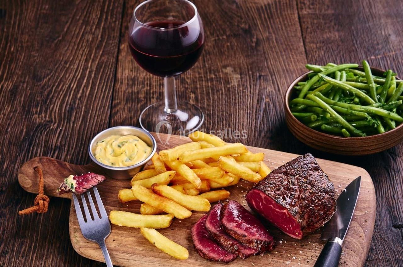 Assiette avec un steak saignant, des frites, une sauce, des haricots verts et un verre de vin rouge sur une table en bois.