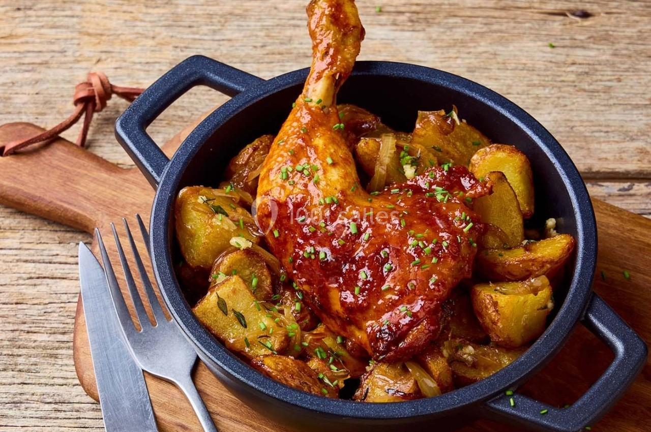 Cuisse de poulet rôtie avec pommes de terre dorées, servie dans une cocotte en fonte sur une planche en bois.