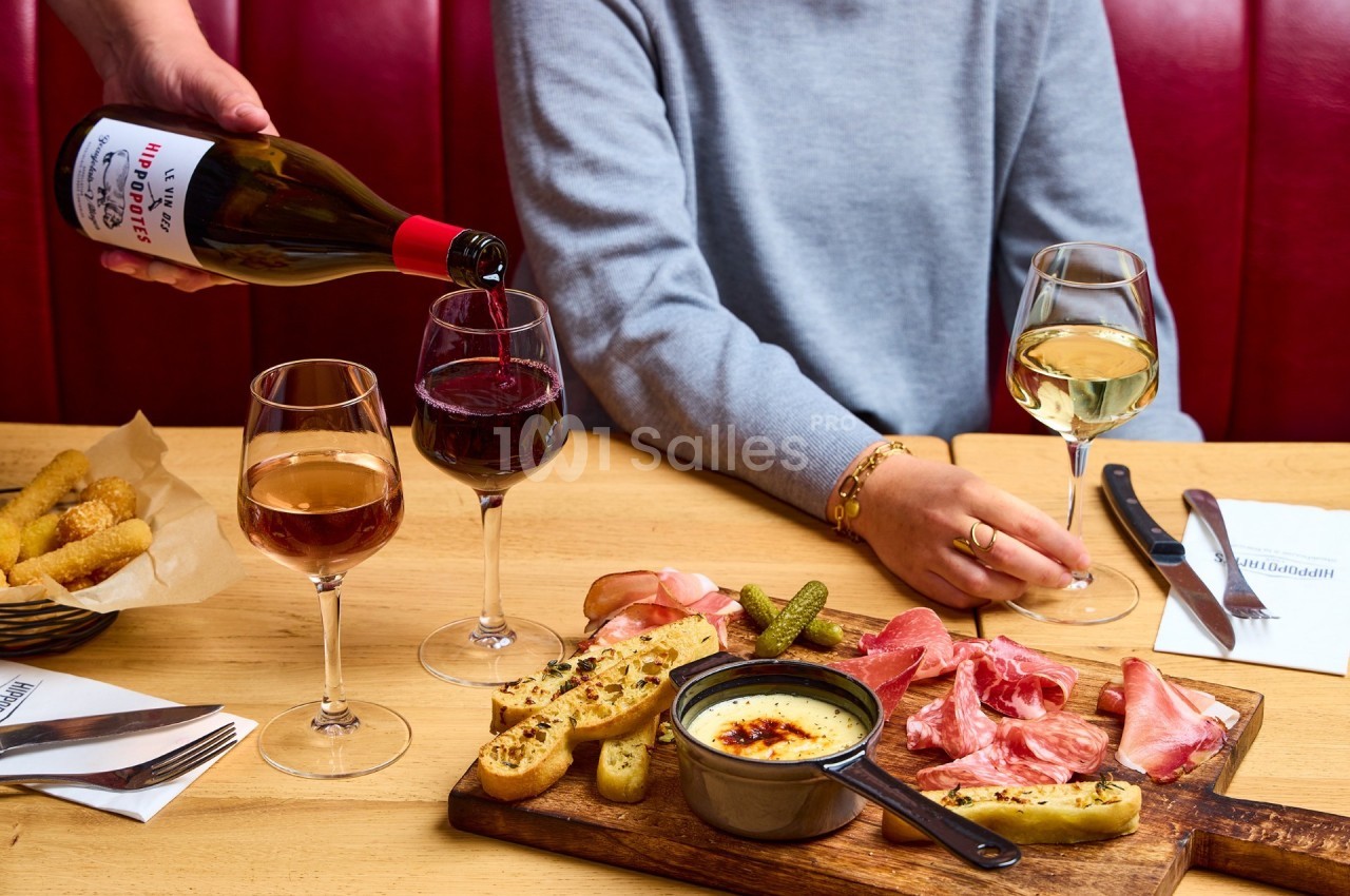 Un serveur verse du vin rouge à table avec des verres de vin et un plateau de charcuterie et fromage.