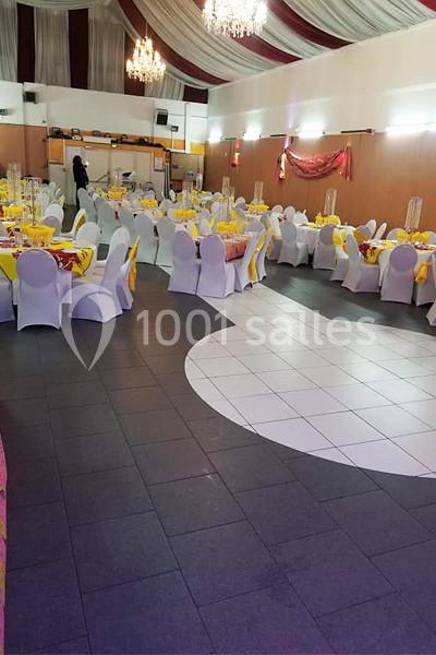 Salle de réception décorée avec des tables rondes dressées de nappes jaunes et rouges, chaises blanches et lustres suspendus.