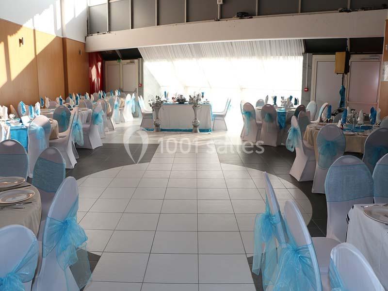 Salle de réception décorée avec des chaises blanches ornées de nœuds bleus et des tables dressées pour un événement.