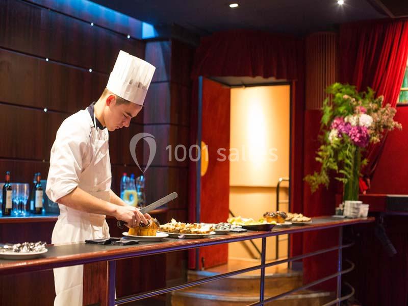 Un chef en tenue blanche découpe un plat sur un buffet dans un cadre élégant avec des fleurs en arrière-plan.