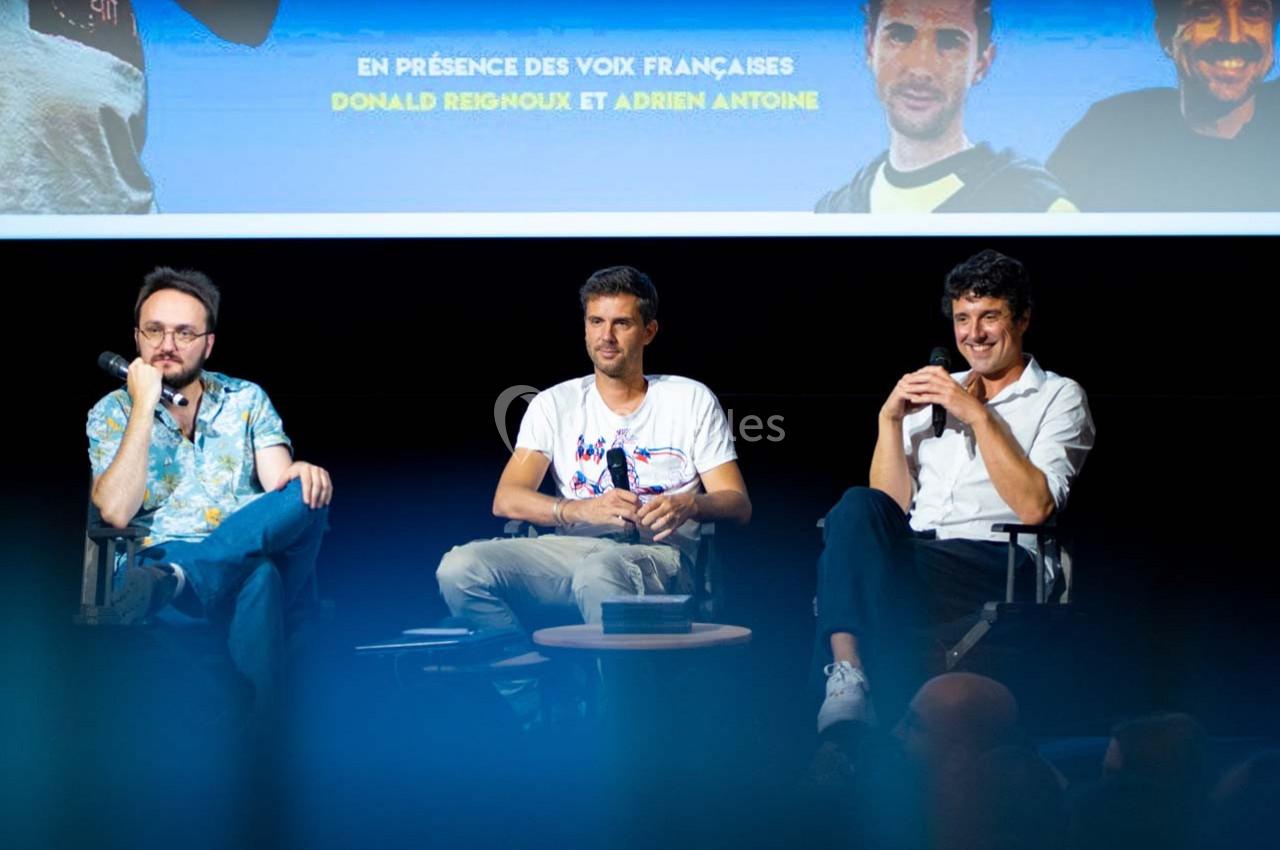 Trois hommes assis sur scène lors d'une discussion, avec un écran projeté en arrière-plan.