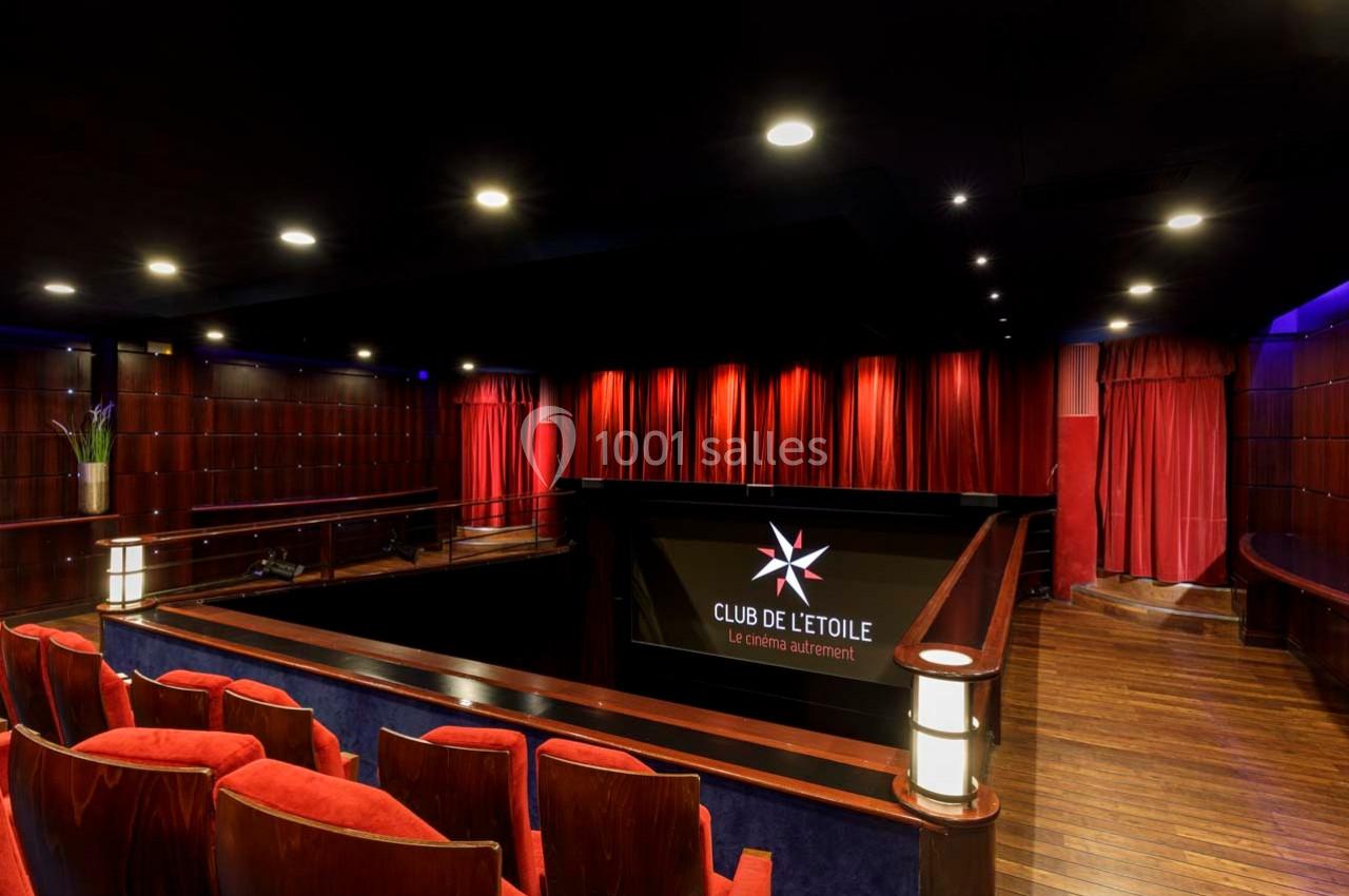 Salle de cinéma avec sièges rouges, rideaux rouges fermés et éclairage tamisé, vue depuis le balcon.