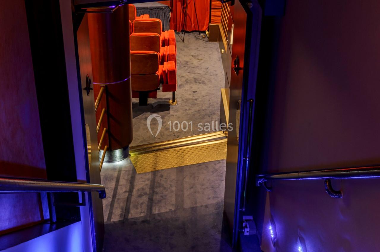 Entrée d'une salle de cinéma avec des sièges rouges visibles à travers une porte ouverte, éclairage tamisé.