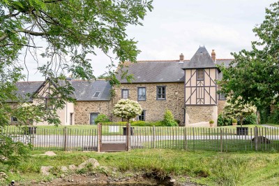 Miniature Façade Manoir @MaudPPhotographie Chambre mansardée avec lit double, poutres apparentes, éclairage chaleureux et fenêtre de toit.