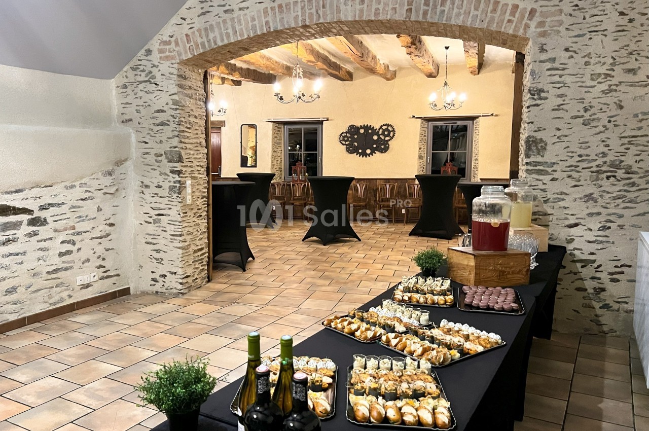 Salle en pierre avec tables dressées pour un buffet, comprenant boissons, verrines et amuse-bouches.