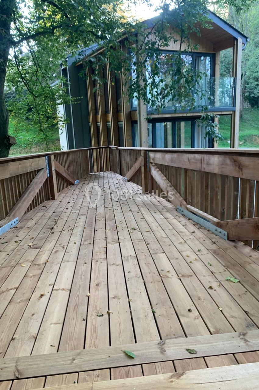 Passerelle en bois menant à une maison moderne entourée d'arbres dans un environnement naturel.