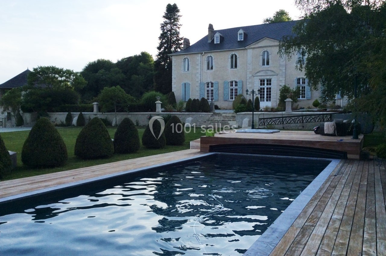 Piscine extérieure en bois devant une grande maison ancienne entourée d'un jardin arboré.