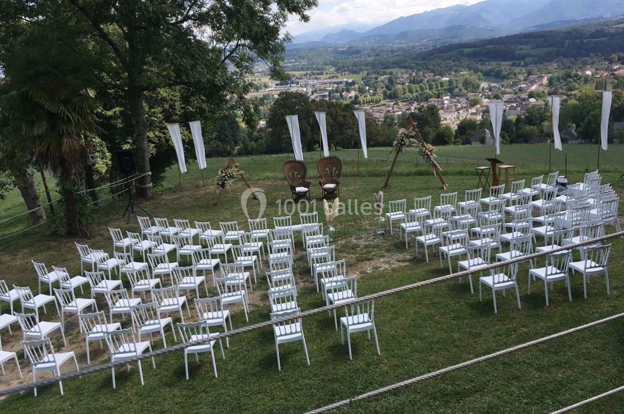 Chaises blanches disposées en extérieur pour une cérémonie, avec une vue sur des collines et une vallée en arrière-plan.