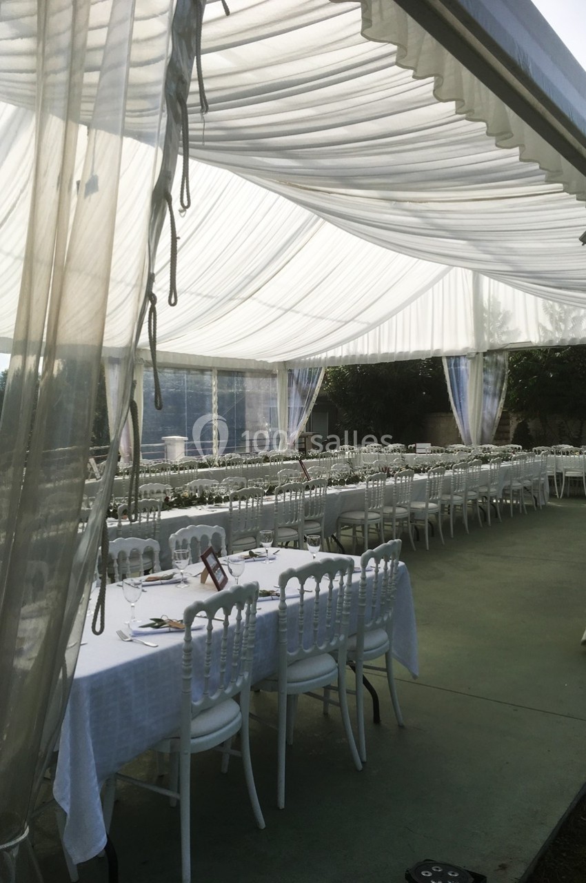 Tables et chaises blanches disposées sous une tente transparente avec un toit en tissu drapé, en extérieur.