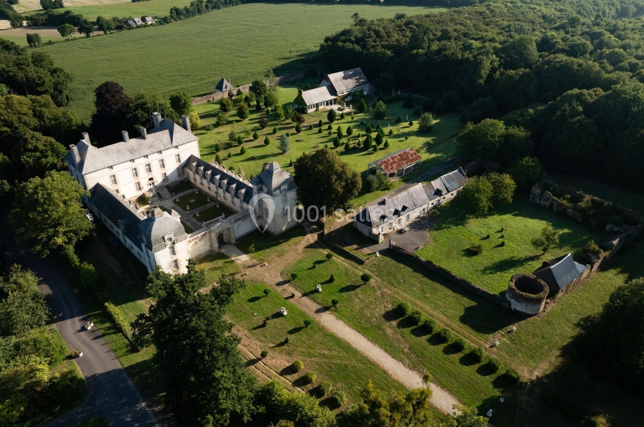 Vue aérienne d'un domaine historique avec bâtiments en pierre, jardins aménagés et forêt environnante.