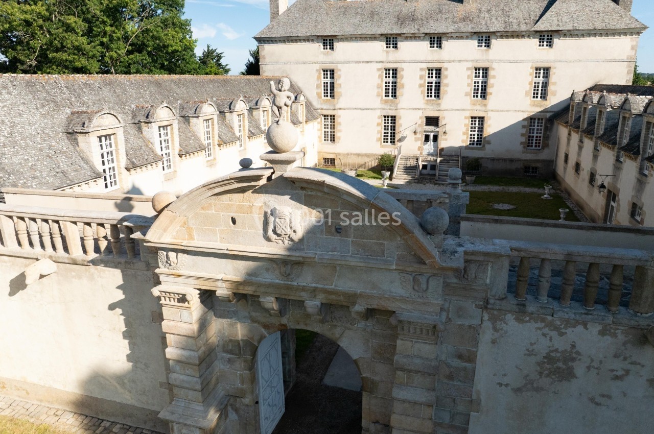 Entrée voûtée en pierre menant à une cour intérieure avec un bâtiment historique en arrière-plan.