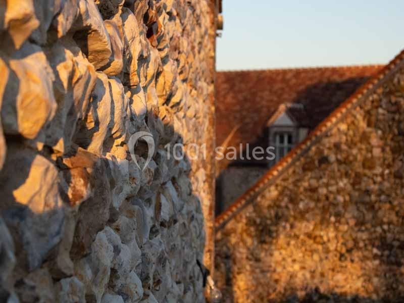 Mur en pierre éclairé par une lumière dorée au coucher du soleil, avec des toits en arrière-plan.