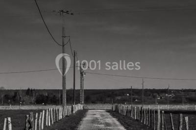 Miniature Location salle Menus (Orne) - Gîte de La Bretillière #15 Chemin de campagne bordé de poteaux électriques et clôtures, traversant un paysage rural sous un ciel sombre.