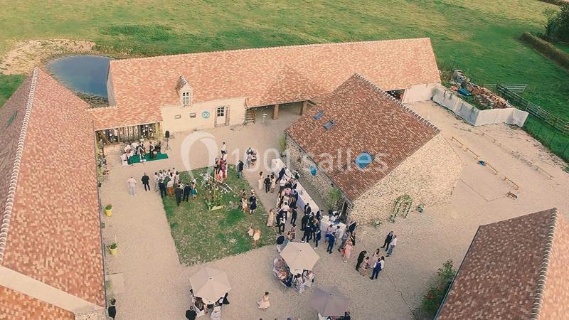 Vue aérienne d'une cour intérieure avec des invités rassemblés pour un événement, entourée de bâtiments en pierre.