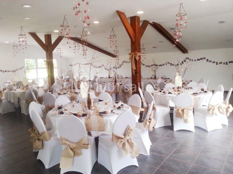 Location salle Saint-Pôtan (Côtes-d'Armor) - La Métairie de la Barre #5 Salle décorée pour un événement avec des tables rondes dressées, nappes blanches et chaises ornées de nœuds beiges.