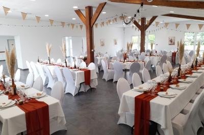 Miniature Location salle Saint-Pôtan (Côtes-d'Armor) - La Métairie de la Barre #14 Table ronde décorée pour un événement, avec nappes beige, chaises blanches ornées de tissu orange et centre de table floral.