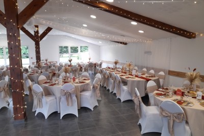 Miniature Location salle Saint-Pôtan (Côtes-d'Armor) - La Métairie de la Barre #30 Table ronde décorée pour un événement, avec nappes beige, chaises blanches ornées de tissu orange et centre de table floral.