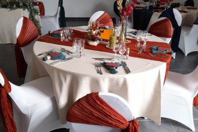 Miniature Location salle Saint-Pôtan (Côtes-d'Armor) - La Métairie de la Barre #32 Table ronde décorée pour un événement, avec nappes beige, chaises blanches ornées de tissu orange et centre de table floral.