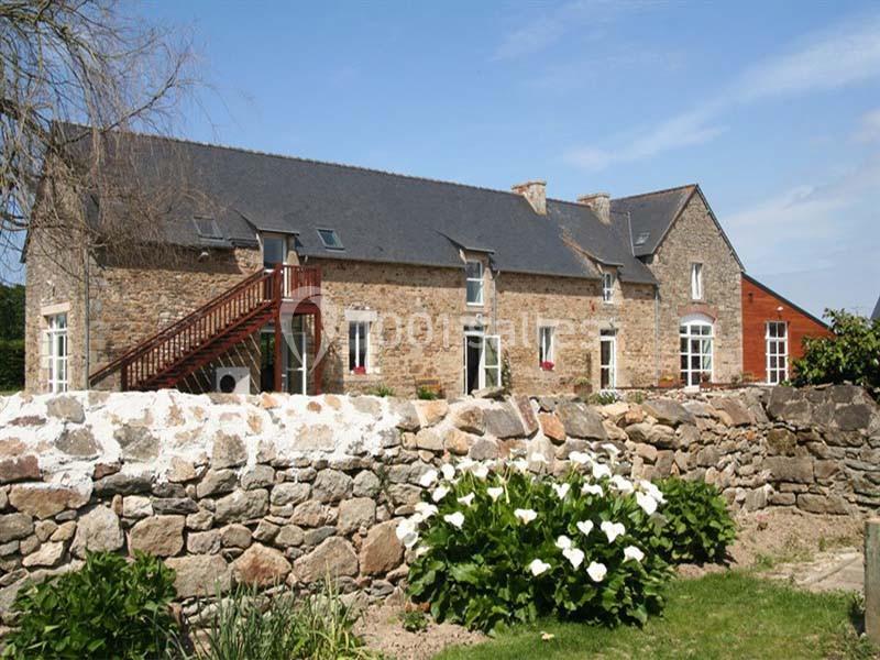 Façade d'une maison en pierre avec toit en ardoise, escalier extérieur en bois et jardin fleuri au premier plan.