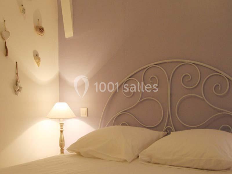 Lit avec tête de lit en métal blanc, mur violet clair, lampe de chevet allumée et décorations murales en forme de cœurs.
