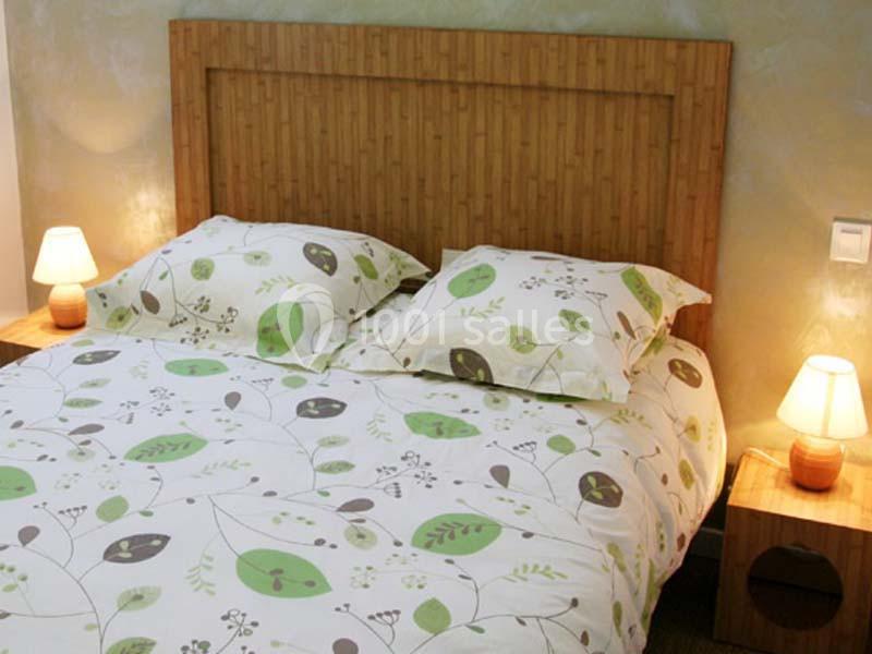 Lit double avec une parure à motifs végétaux verts et blancs, encadré par deux tables de chevet avec lampes allumées.