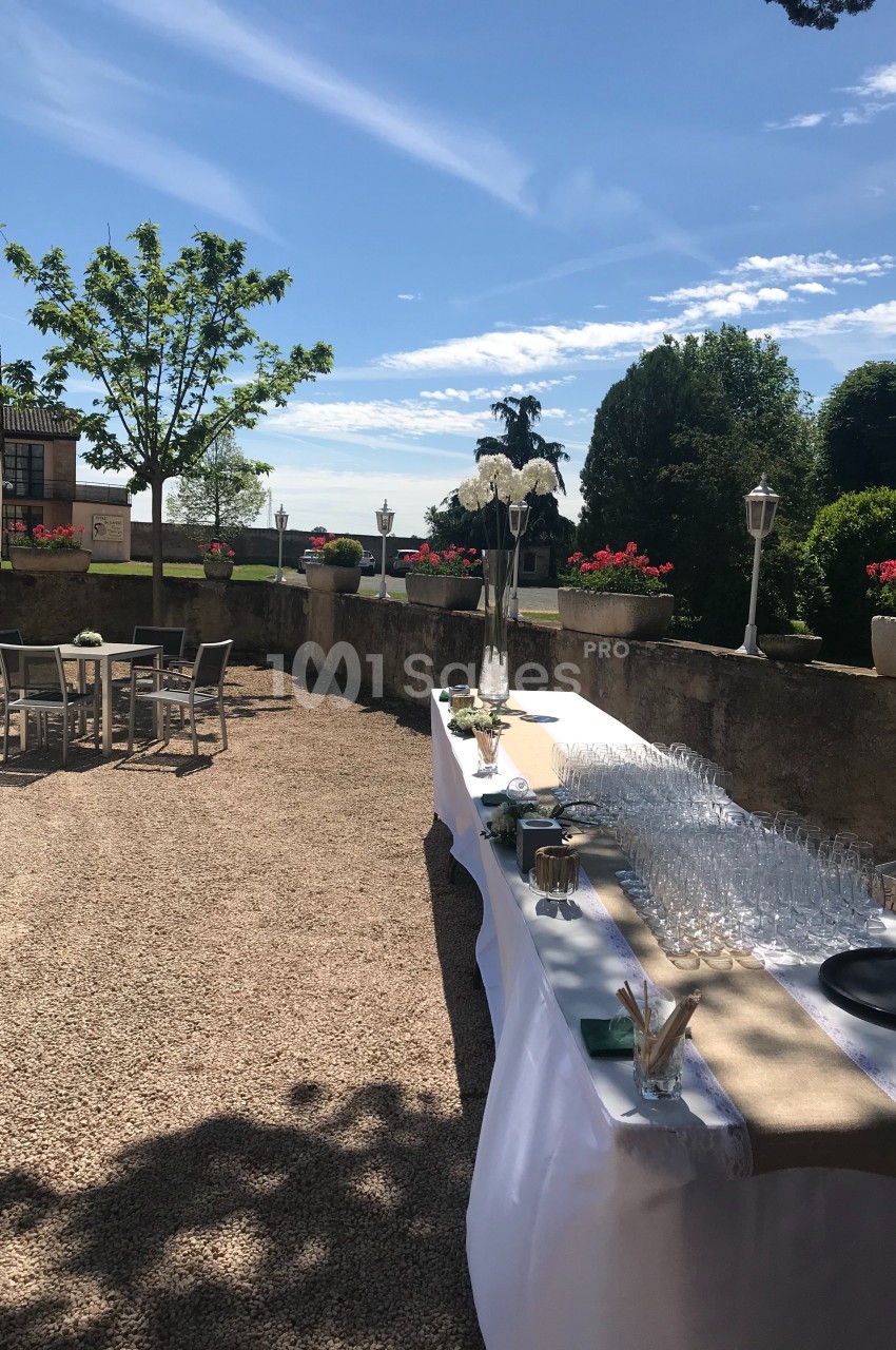 Table dressée avec verres et décorations sur une terrasse ensoleillée, entourée de végétation et de mobilier extérieur.
