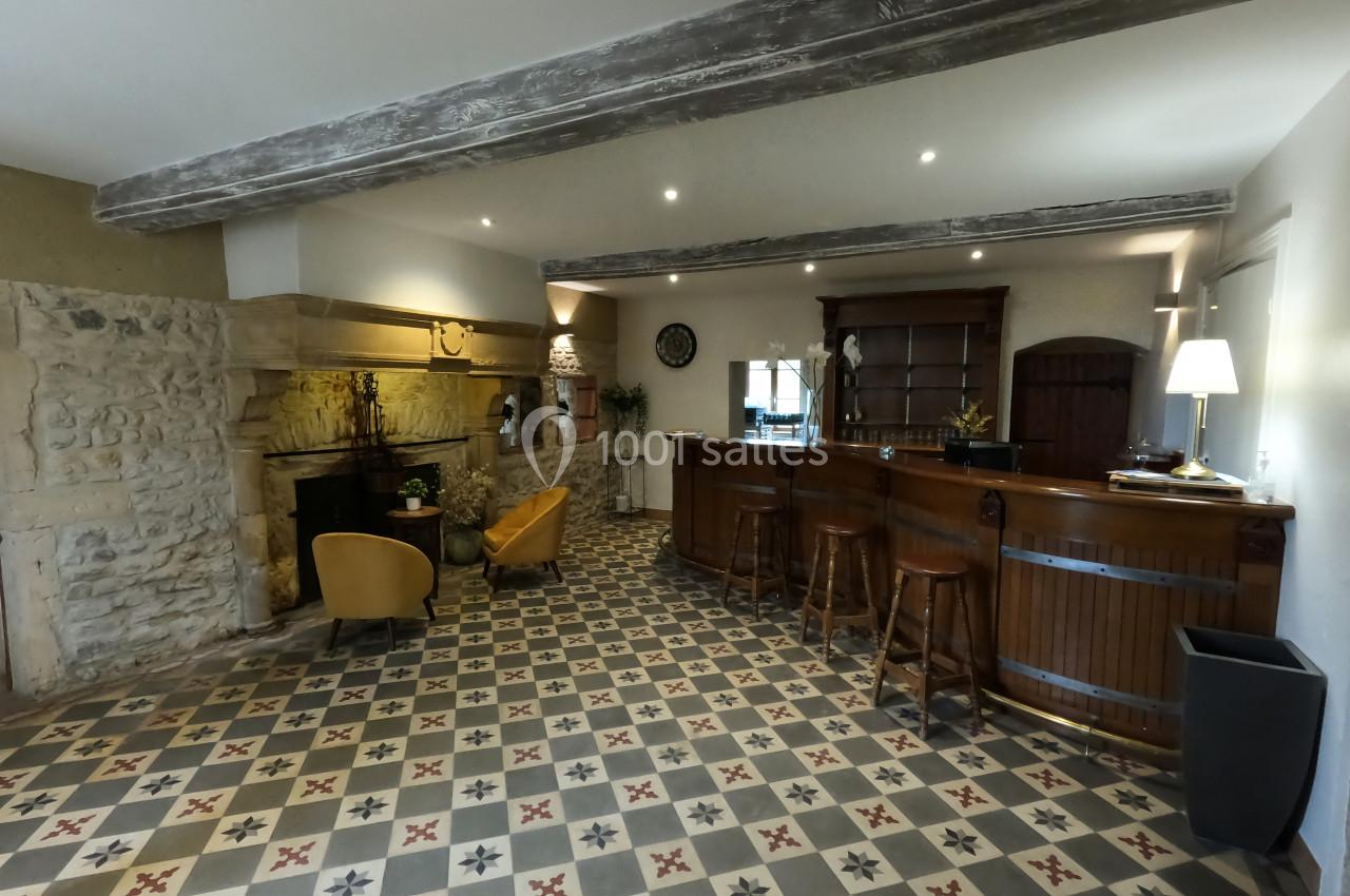 Salle avec un bar en bois, cheminée en pierre, fauteuils jaunes et carrelage à motifs géométriques.