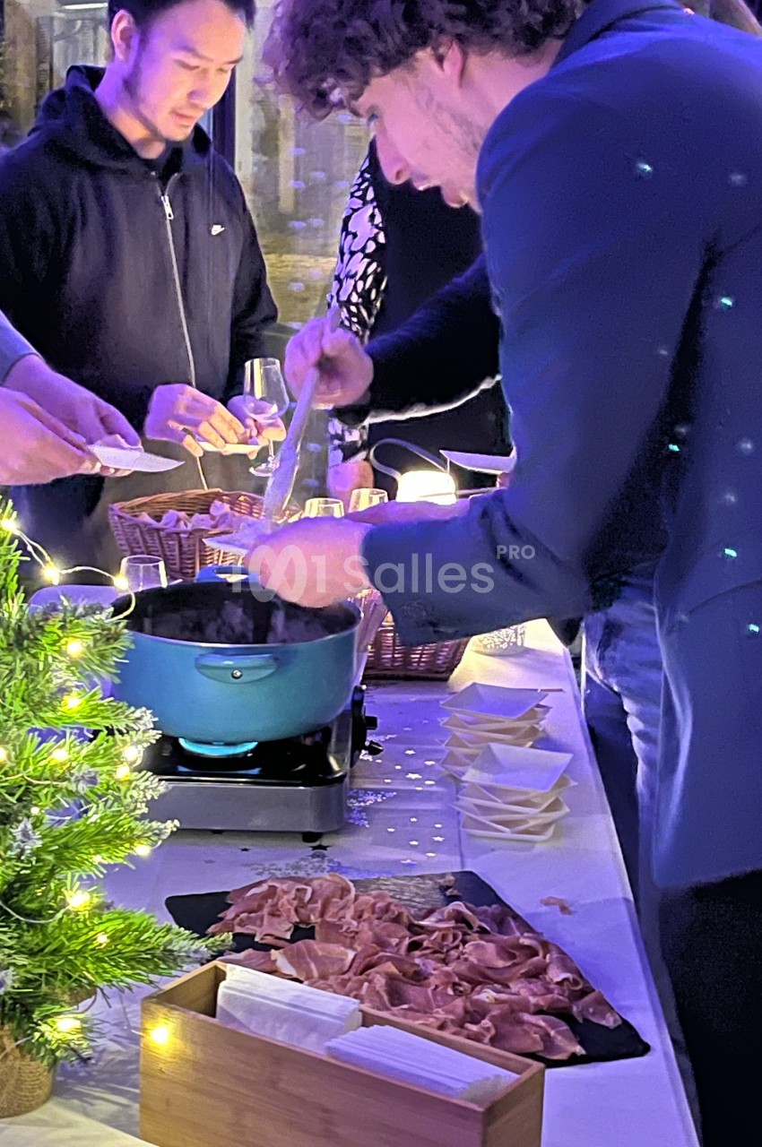 Un homme sert un plat chaud dans une ambiance conviviale, avec des tranches de charcuterie disposées sur une table éclairée.