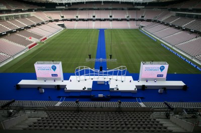 Salle lumineuse avec fauteuils rouges, table basse en verre, écran mural et baie vitrée donnant sur l'extérieur.