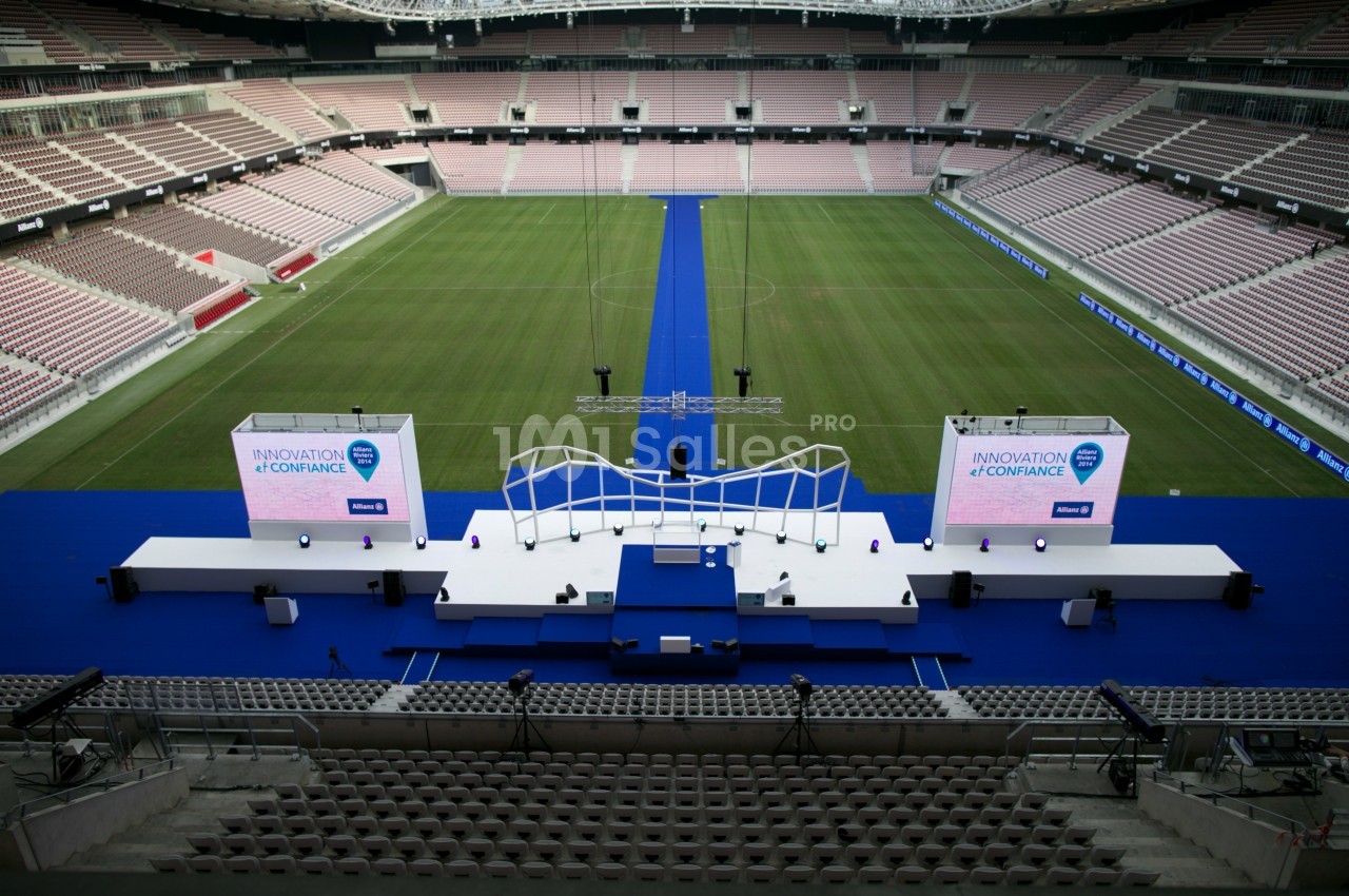 Scène blanche avec écrans et décor moderne installée sur un terrain de stade, entourée de gradins vides.