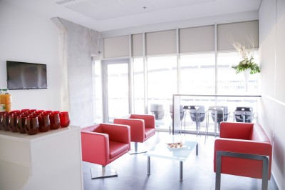 Salle lumineuse avec fauteuils rouges, table basse en verre, écran mural et baie vitrée donnant sur l'extérieur.