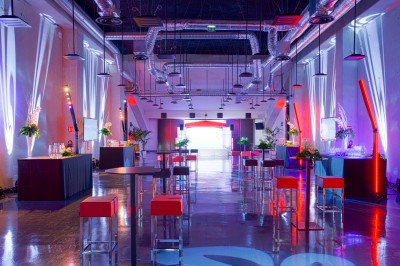 Salle lumineuse avec fauteuils rouges, table basse en verre, écran mural et baie vitrée donnant sur l'extérieur.