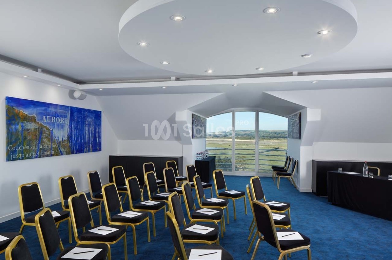 Salle de conférence lumineuse avec chaises alignées, fenêtres offrant une vue sur un paysage verdoyant.