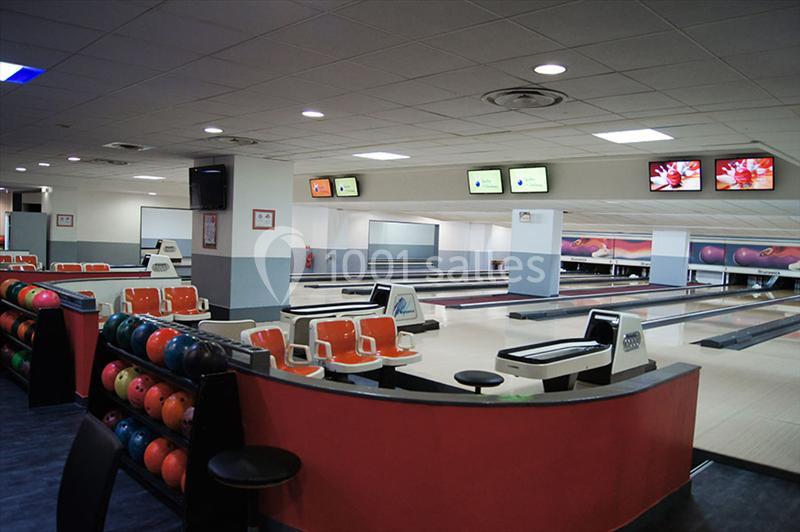 Salle de bowling avec plusieurs pistes, des écrans suspendus et des rangées de boules colorées rangées sur le côté.