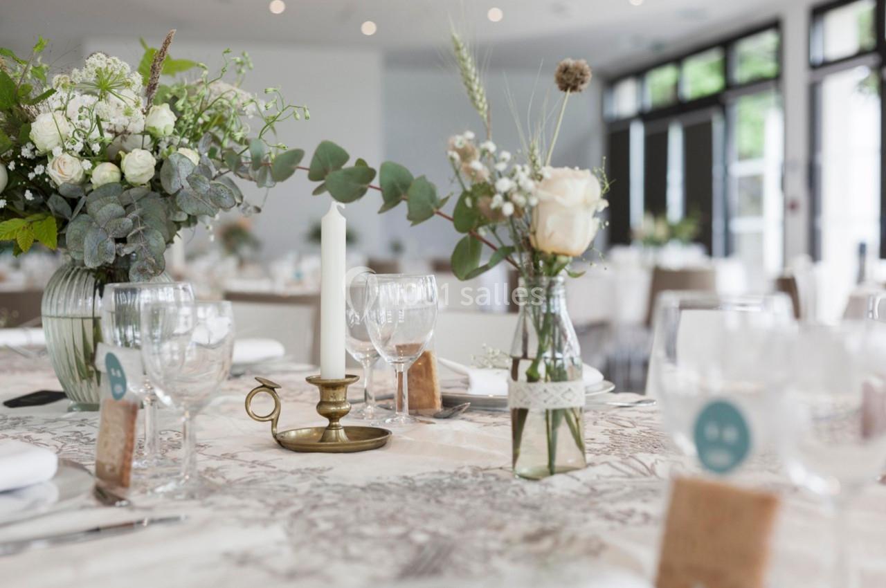 Table décorée avec des fleurs, bougeoir en laiton et vaisselle élégante dans une salle lumineuse.