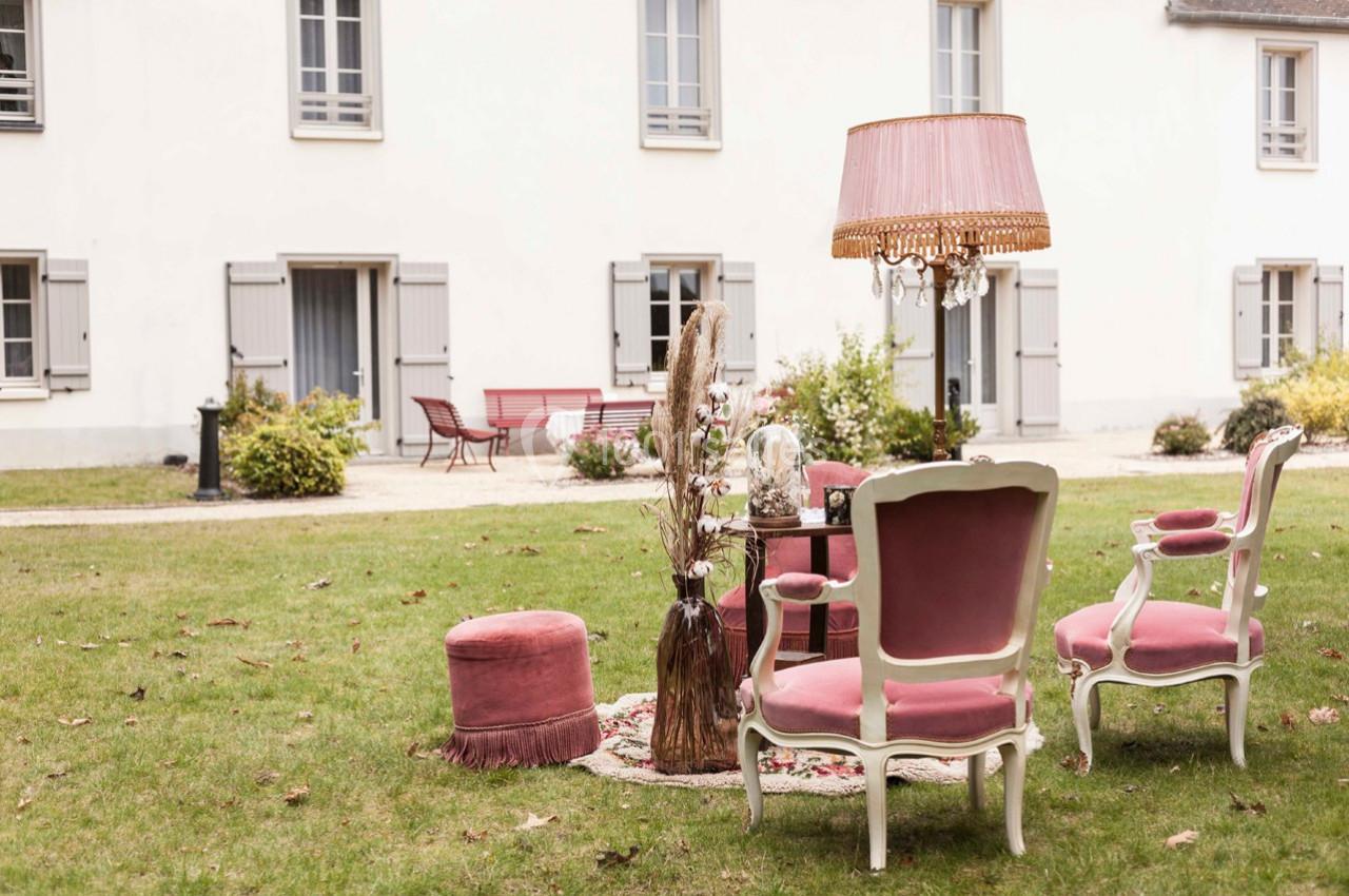 Mobilier de salon vintage avec fauteuils roses et lampe posés sur une pelouse devant une maison blanche.