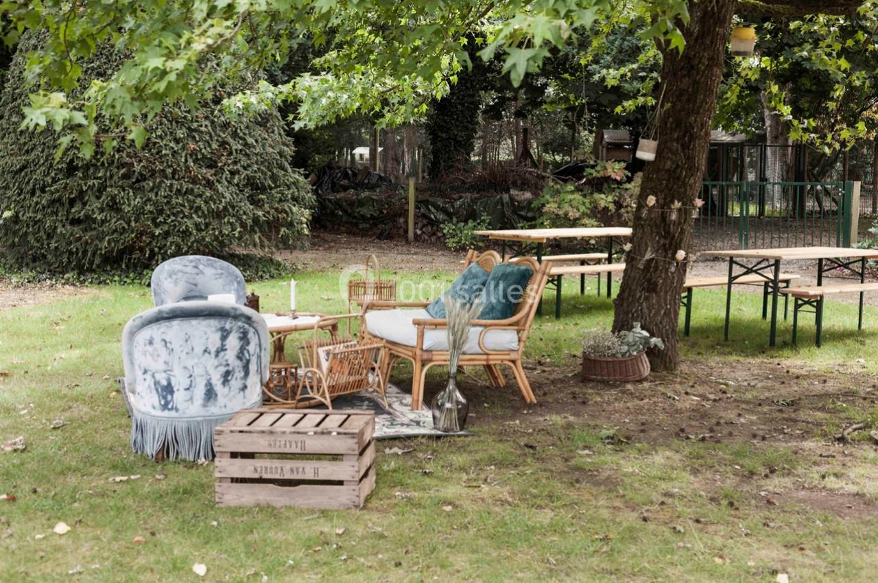 Mobilier de jardin composé de fauteuils, tables et caisses en bois, installé sous un arbre dans un espace extérieur…