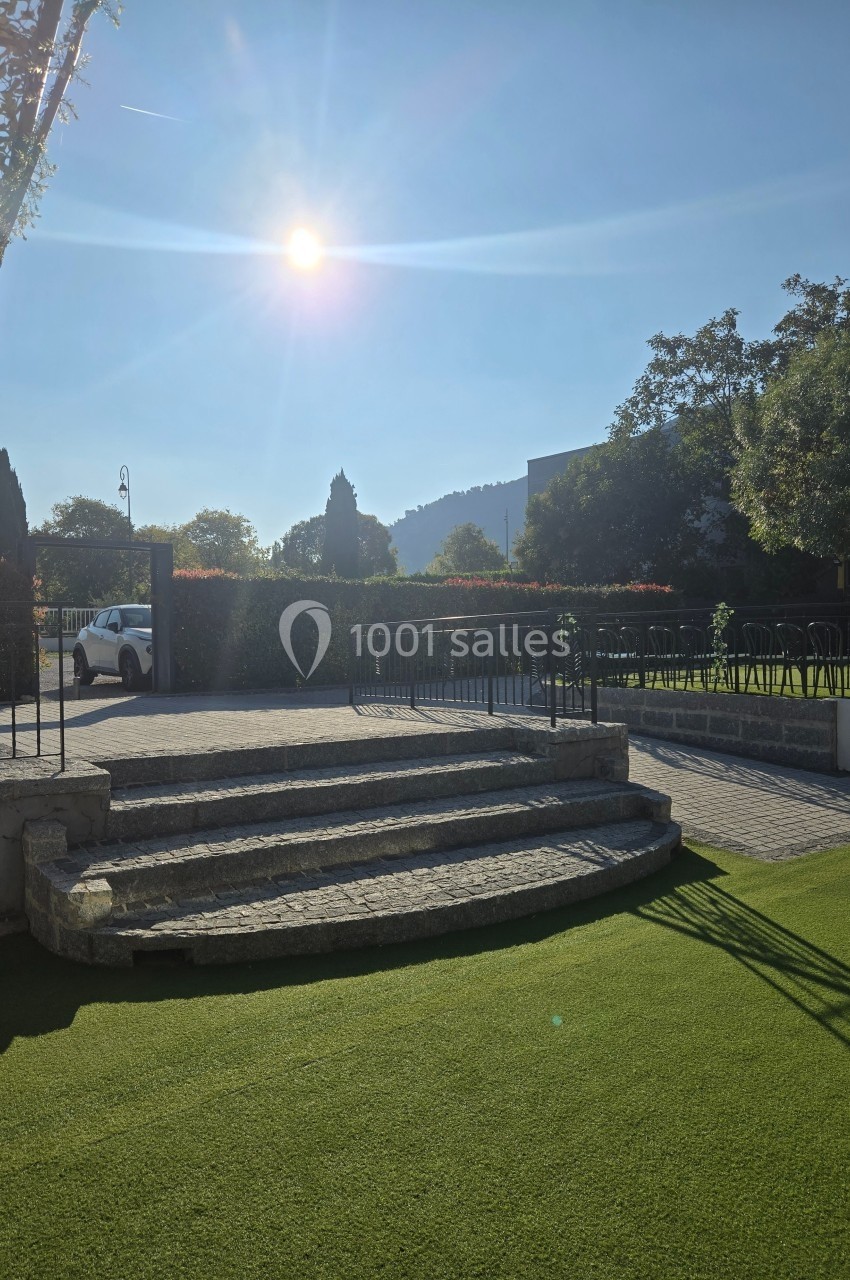 Escalier en pierre menant à une terrasse ensoleillée, entourée de verdure et d'arbres sous un ciel dégagé.