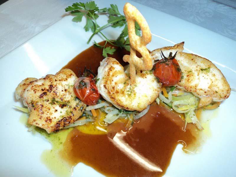 Assiette de poisson grillé avec légumes, tomates cerises rôties, sauce brune et décoration en pâte croustillante.