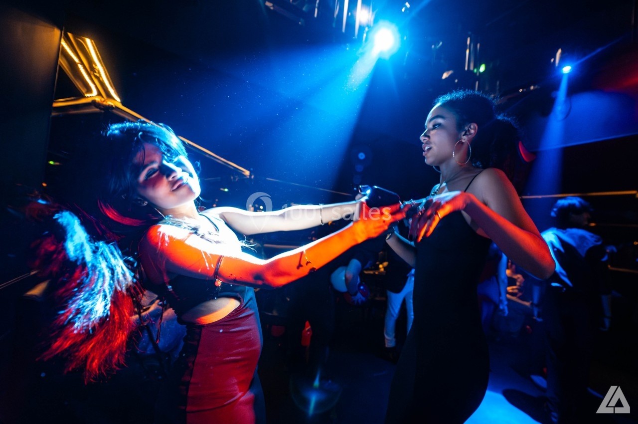 Deux femmes dansent sous des lumières colorées dans une ambiance festive de boîte de nuit.