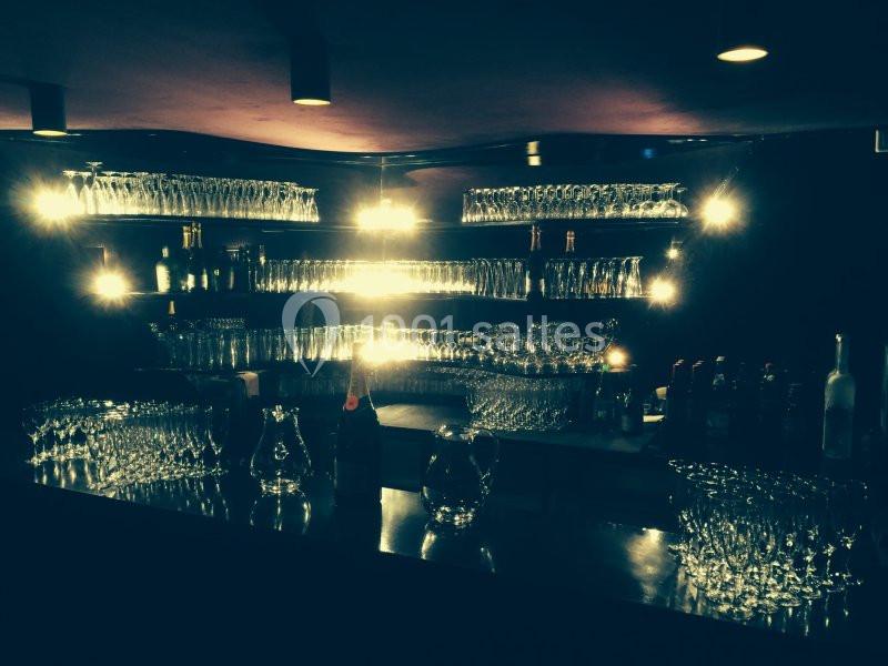 Un bar sombre avec des étagères remplies de verres éclairés par des lumières tamisées.